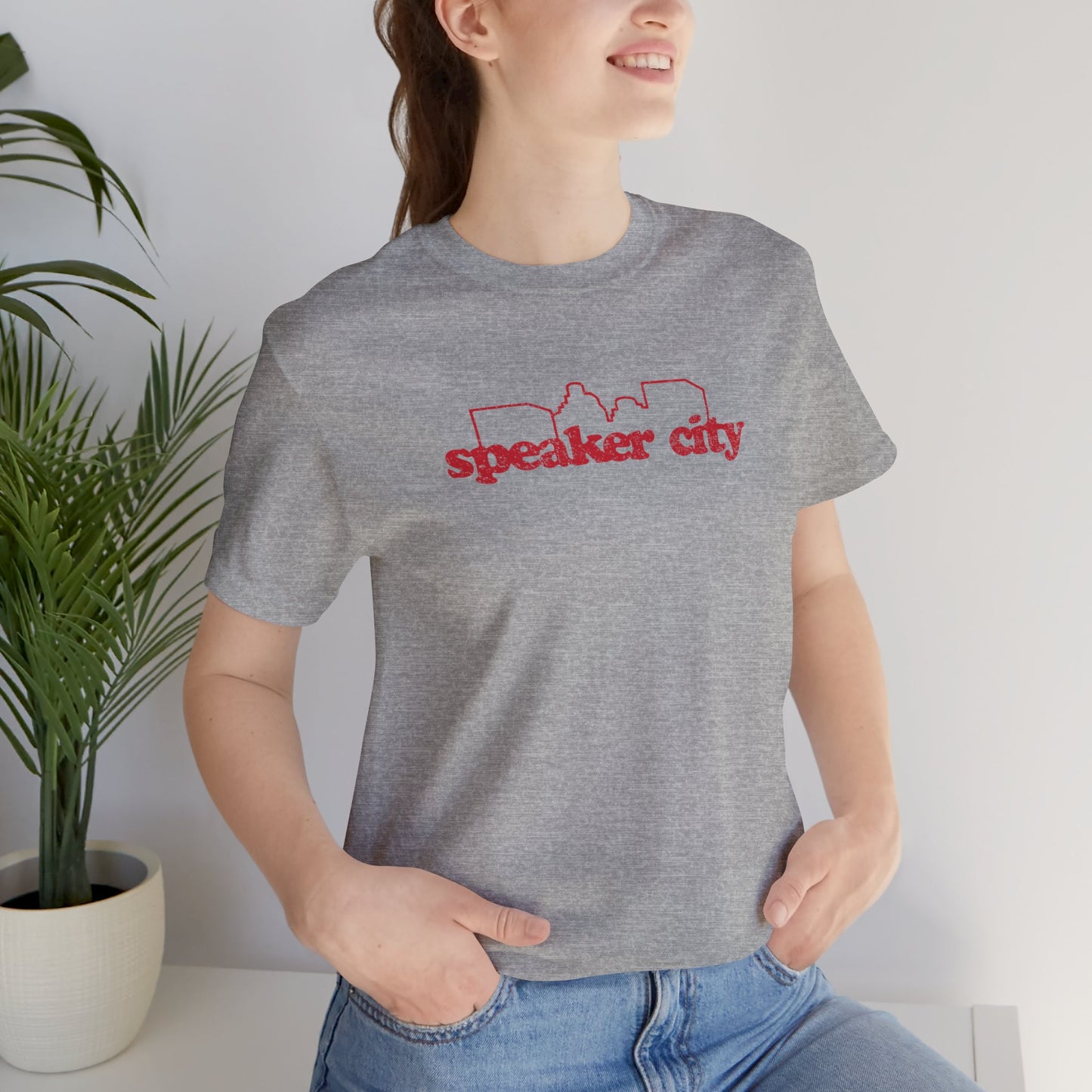 female wearing grey t-shirt featuring the Speaker City logo from the movie Old School in a vintage distressed style with red print and skyline outline.