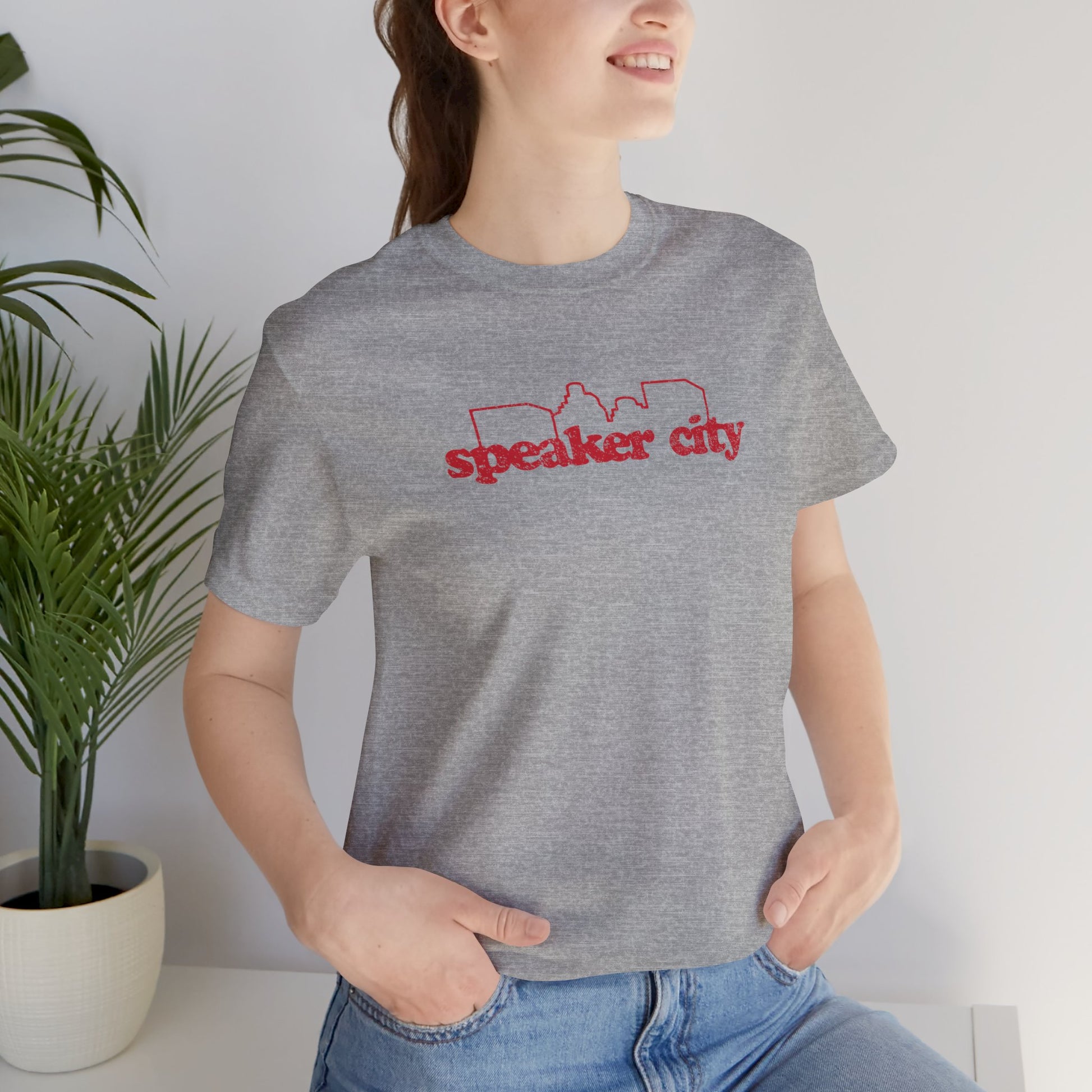 female wearing grey t-shirt featuring the Speaker City logo from the movie Old School in a vintage distressed style with red print and skyline outline.