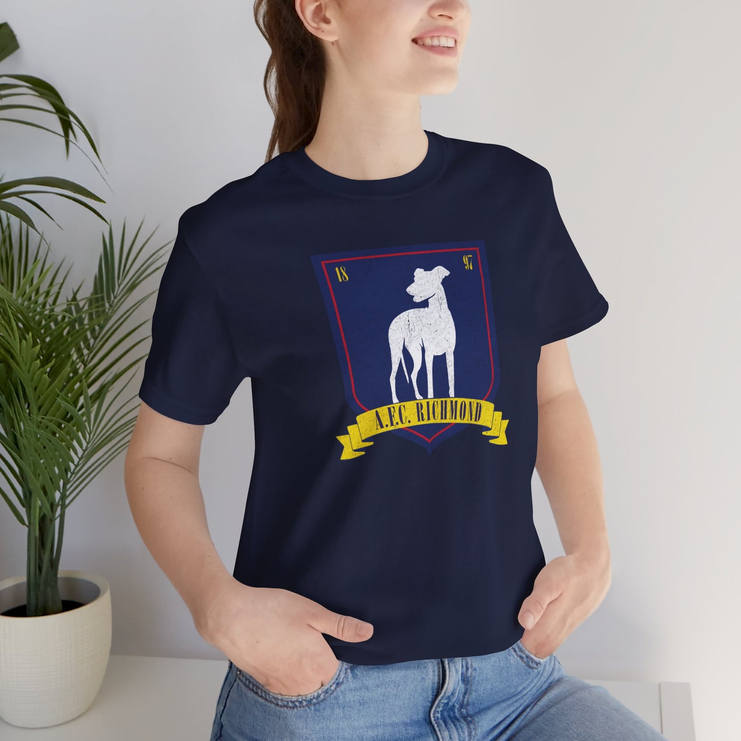 Female model wearing a navy blue soft Bella+Canvas 3001 short-sleeve t-shirt featuring the logo graphic of the fictional English soccer team AFC Richmond inspired by the TV show Ted Lasso in a vintage distressed style, sold by ScriptedBrand.