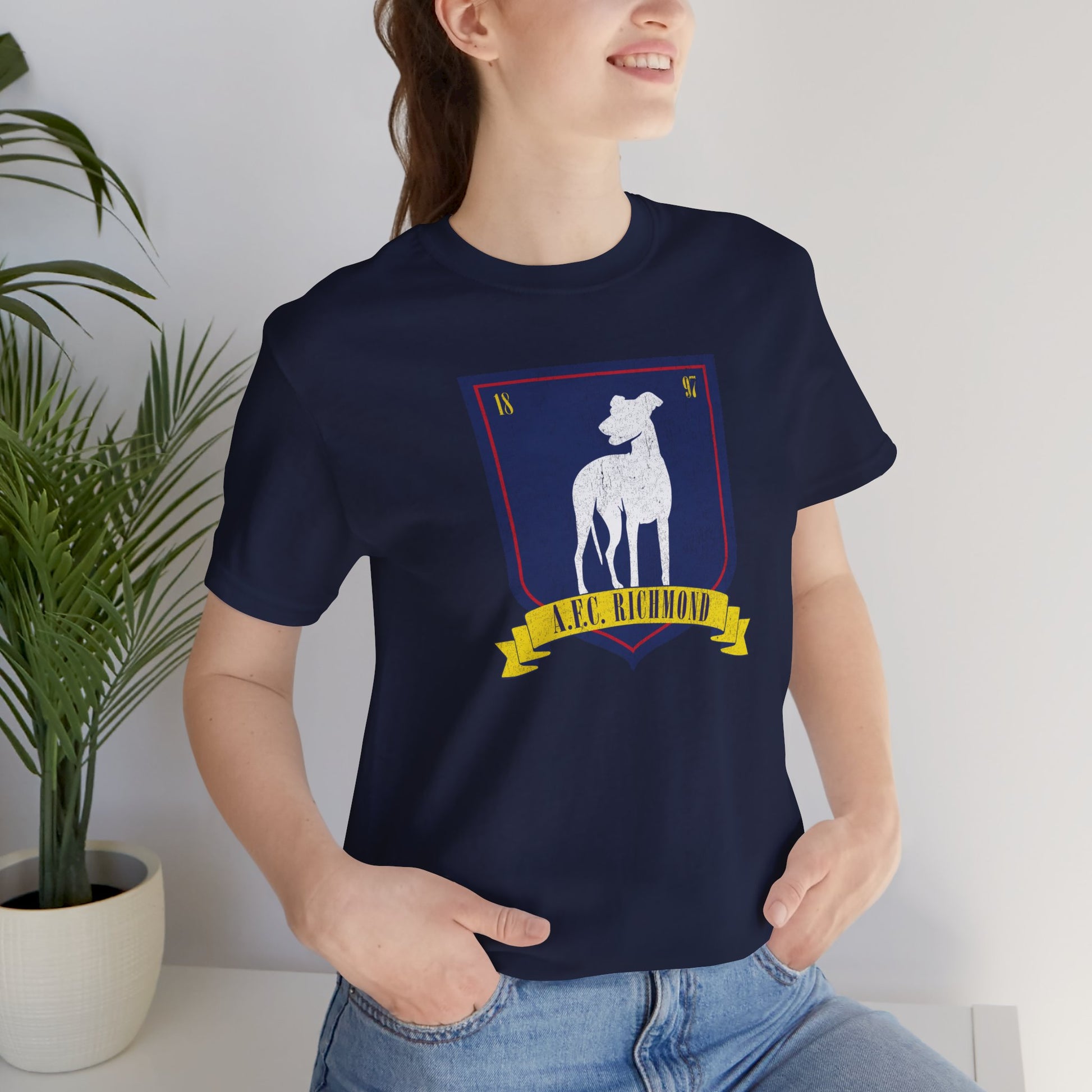 Female model wearing a navy blue soft Bella+Canvas 3001 short-sleeve t-shirt featuring the logo graphic of the fictional English soccer team AFC Richmond inspired by the TV show Ted Lasso in a vintage distressed style, sold by ScriptedBrand.