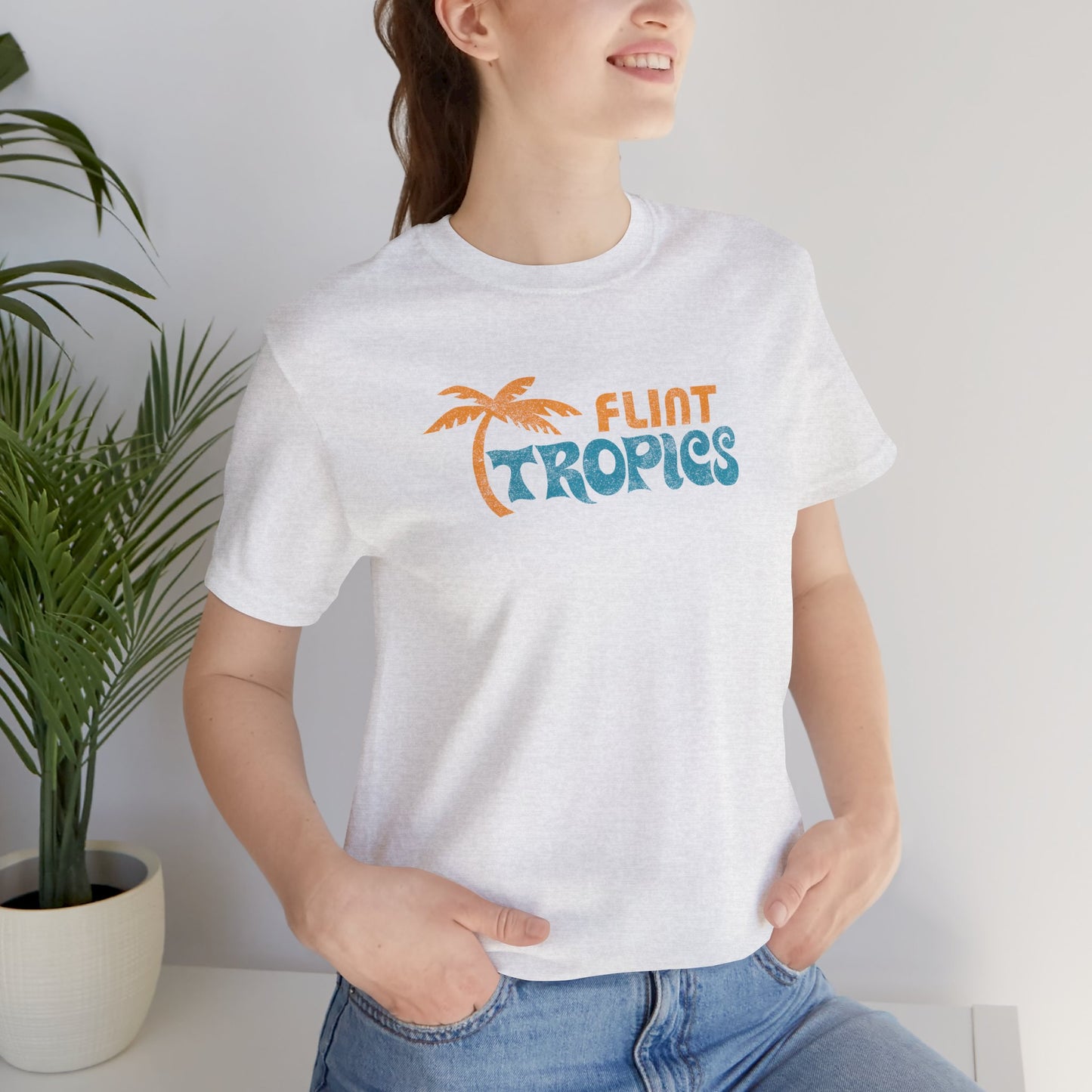Female model wearing a white colored soft Bella+Canvas 3001 short-sleeve t-shirt tee featuring the Flint Tropics logo from the movie Semi-Pro, in a vintage distressed style, sold by ScriptedBrand.