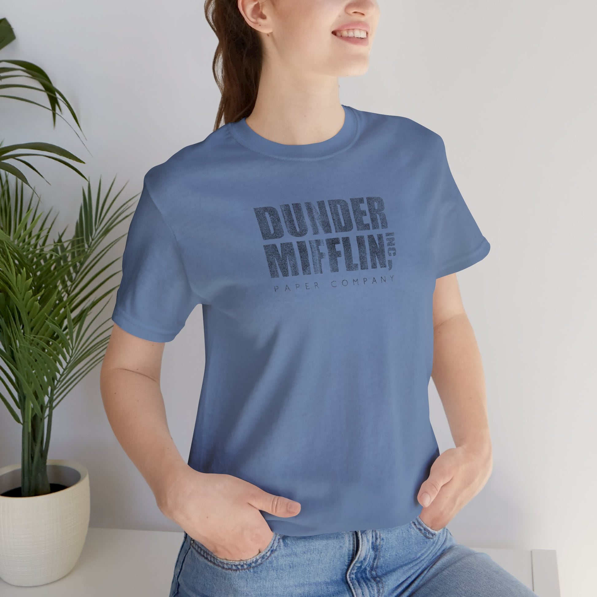 Woman wearing a steel blue t-shirt featuring the Dunder Mifflin logo from the TV show The Office in a vintage distressed style.
