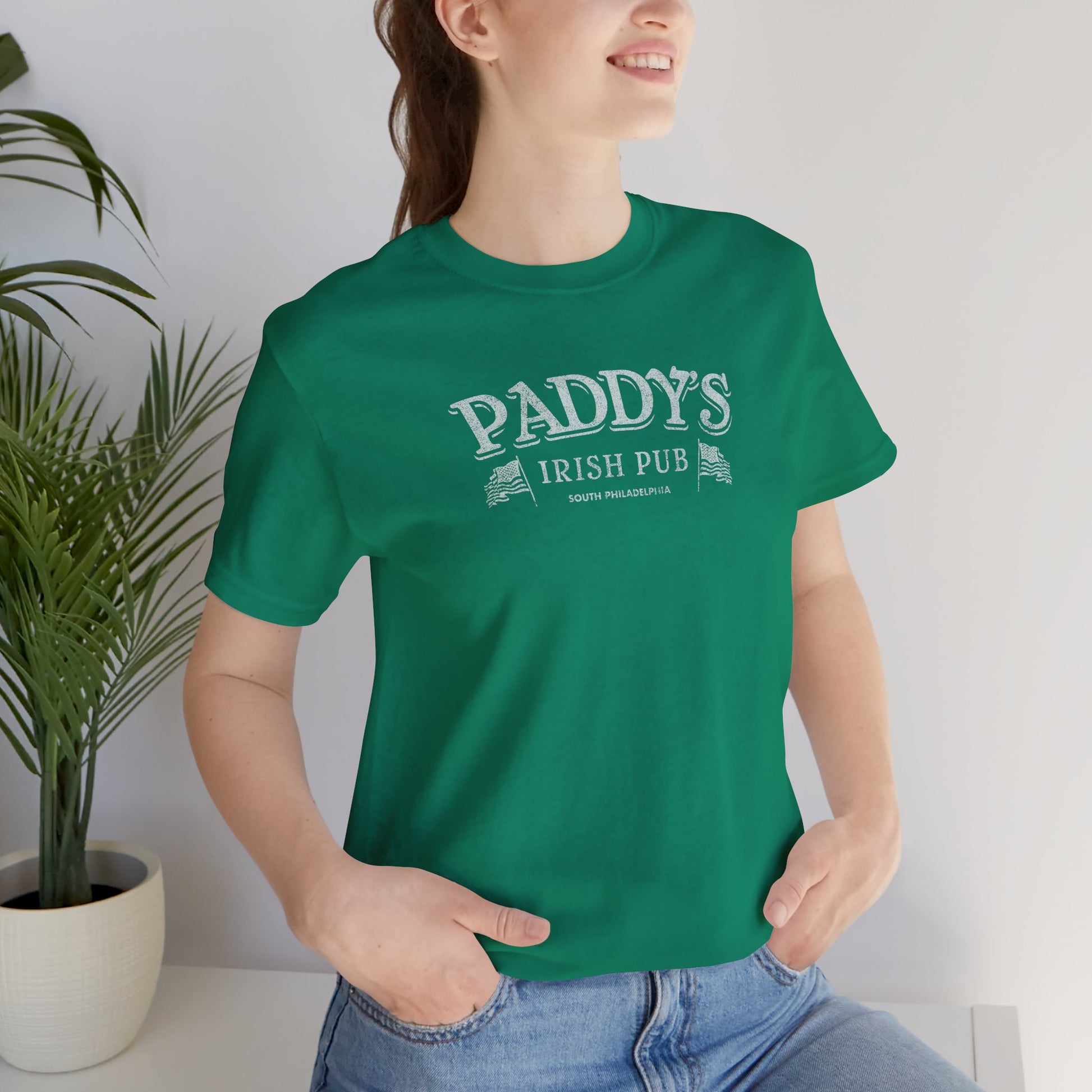 Female model wearing a kelly green colored soft Bella+Canvas 3001 short-sleeve t-shirt tee featuring the Paddy's Pub logo from the TV Show It's Always Sunny in Philadelphia, in a vintage distressed style, sold by ScriptedBrand.