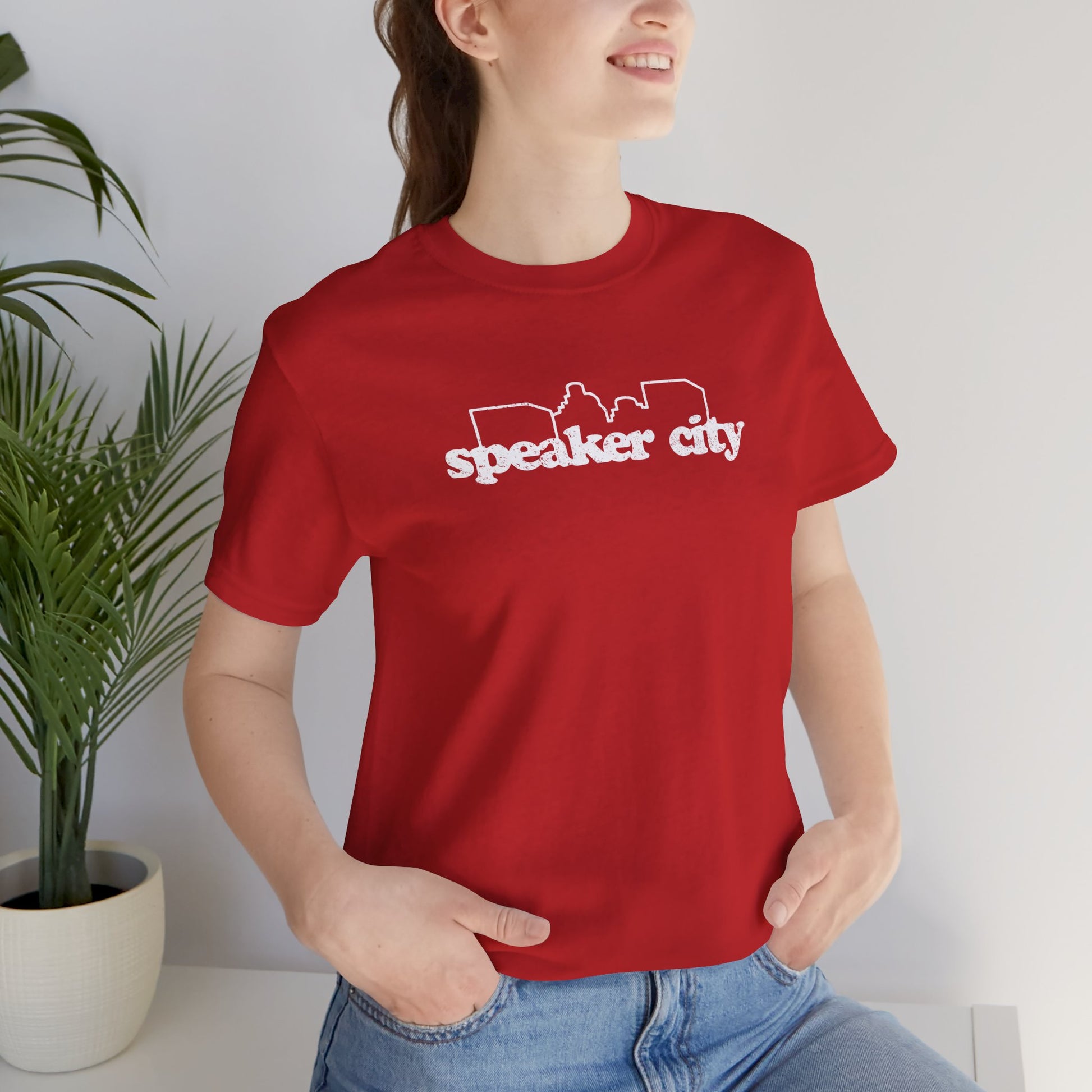 female wearing red t-shirt featuring the Speaker City logo from the movie Old School in a vintage distressed style with white print and skyline outline.