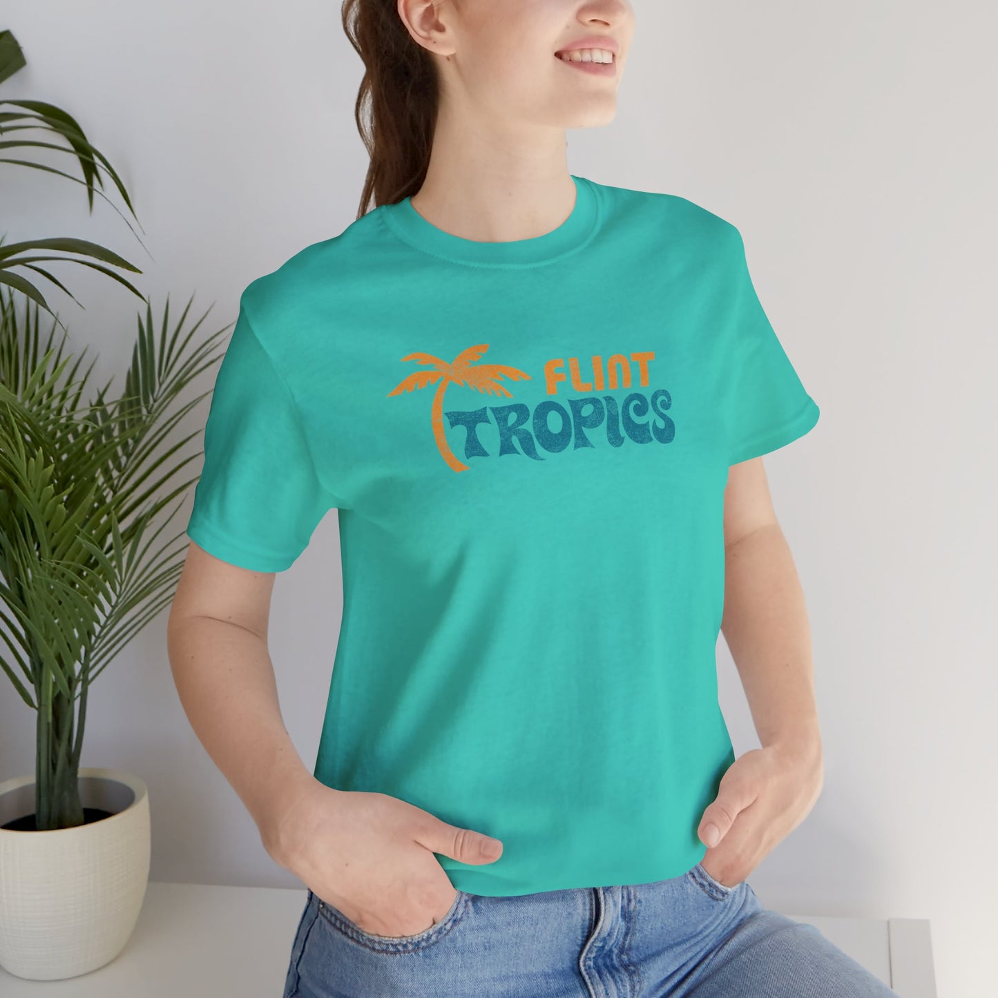 Female model wearing a teal colored soft Bella+Canvas 3001 short-sleeve t-shirt tee featuring the Flint Tropics logo from the movie Semi-Pro, in a vintage distressed style, sold by ScriptedBrand.
