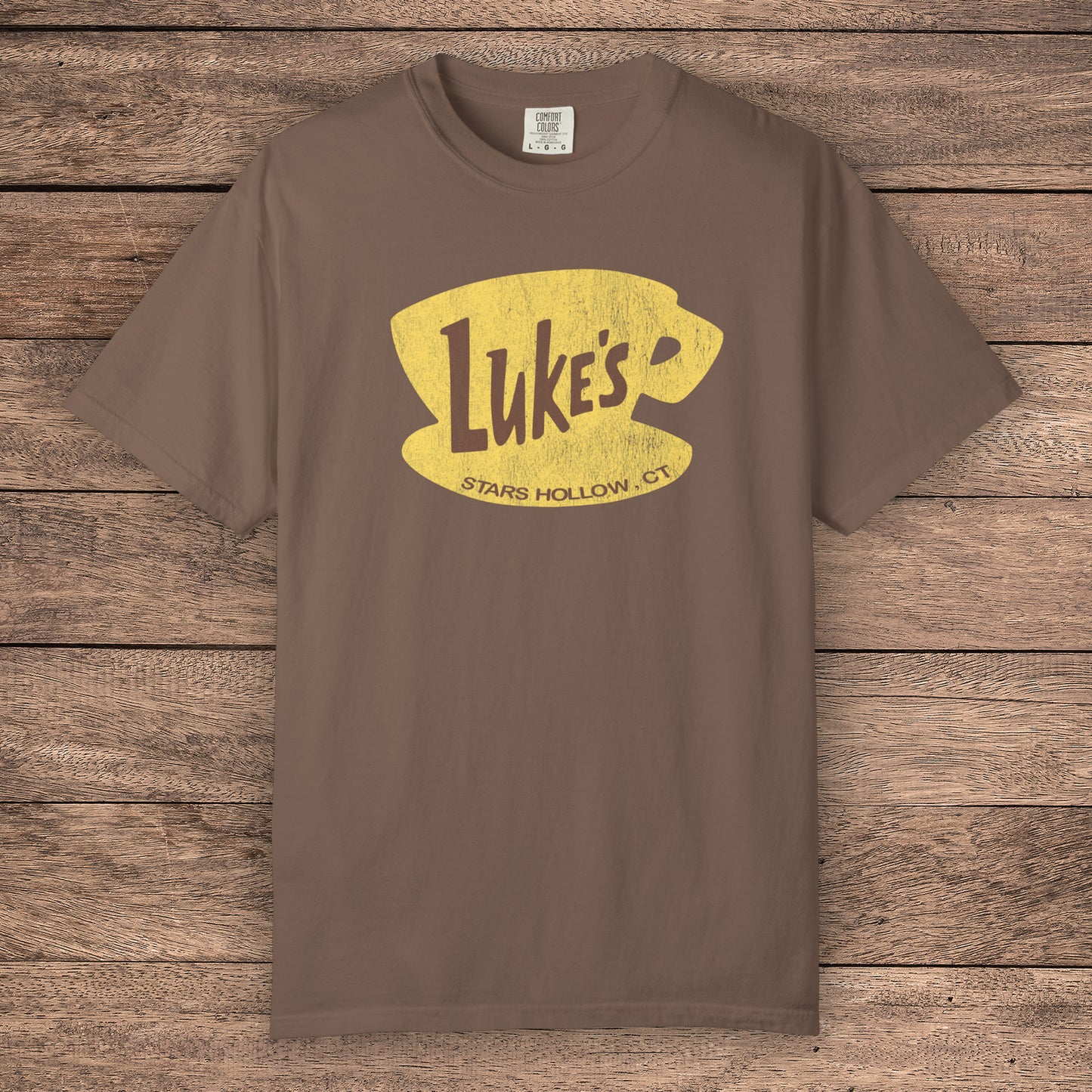 Espresso brown Comfort Colors t-shirt with vintage yellow Luke’s Diner logo from Gilmore Girls, laid flat on wood background.