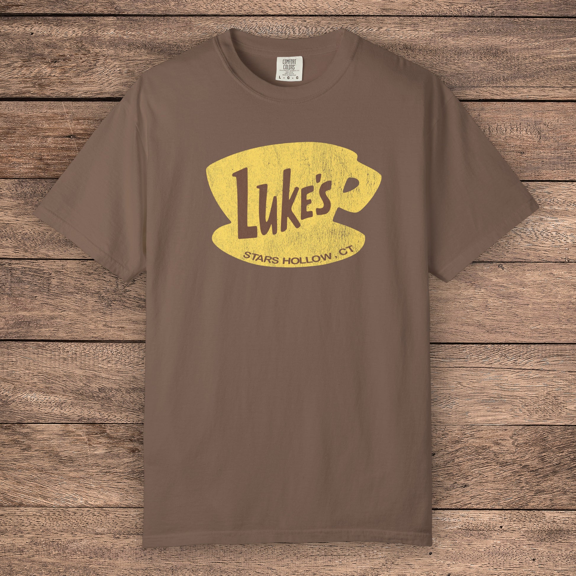Espresso brown Comfort Colors t-shirt with vintage yellow Luke’s Diner logo from Gilmore Girls, laid flat on wood background.