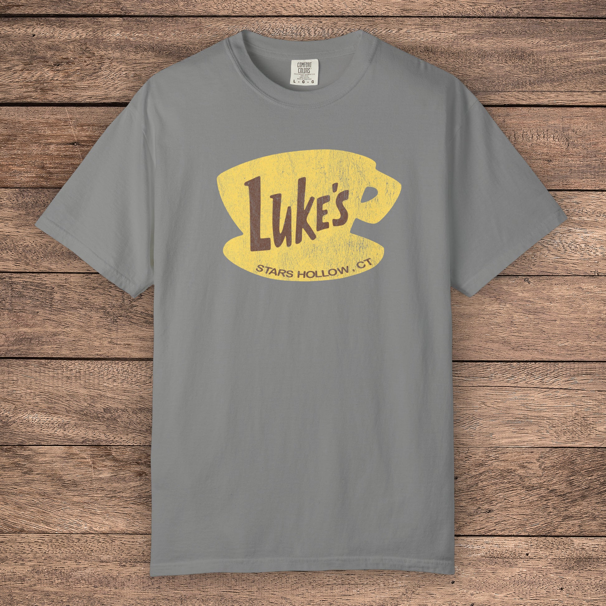Granite Gray Comfort Colors t-shirt with vintage yellow Luke’s Diner logo from Gilmore Girls, laid flat on wood background.