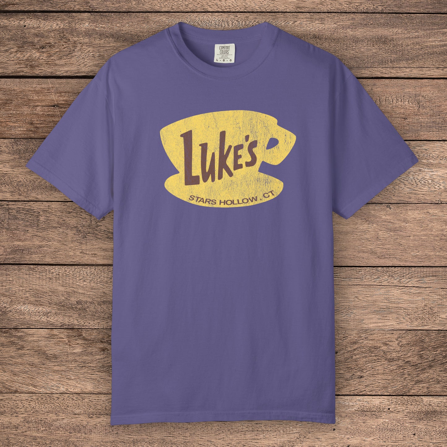 Grape Purple Comfort Colors t-shirt with vintage yellow Luke’s Diner logo from Gilmore Girls, laid flat on wood background.