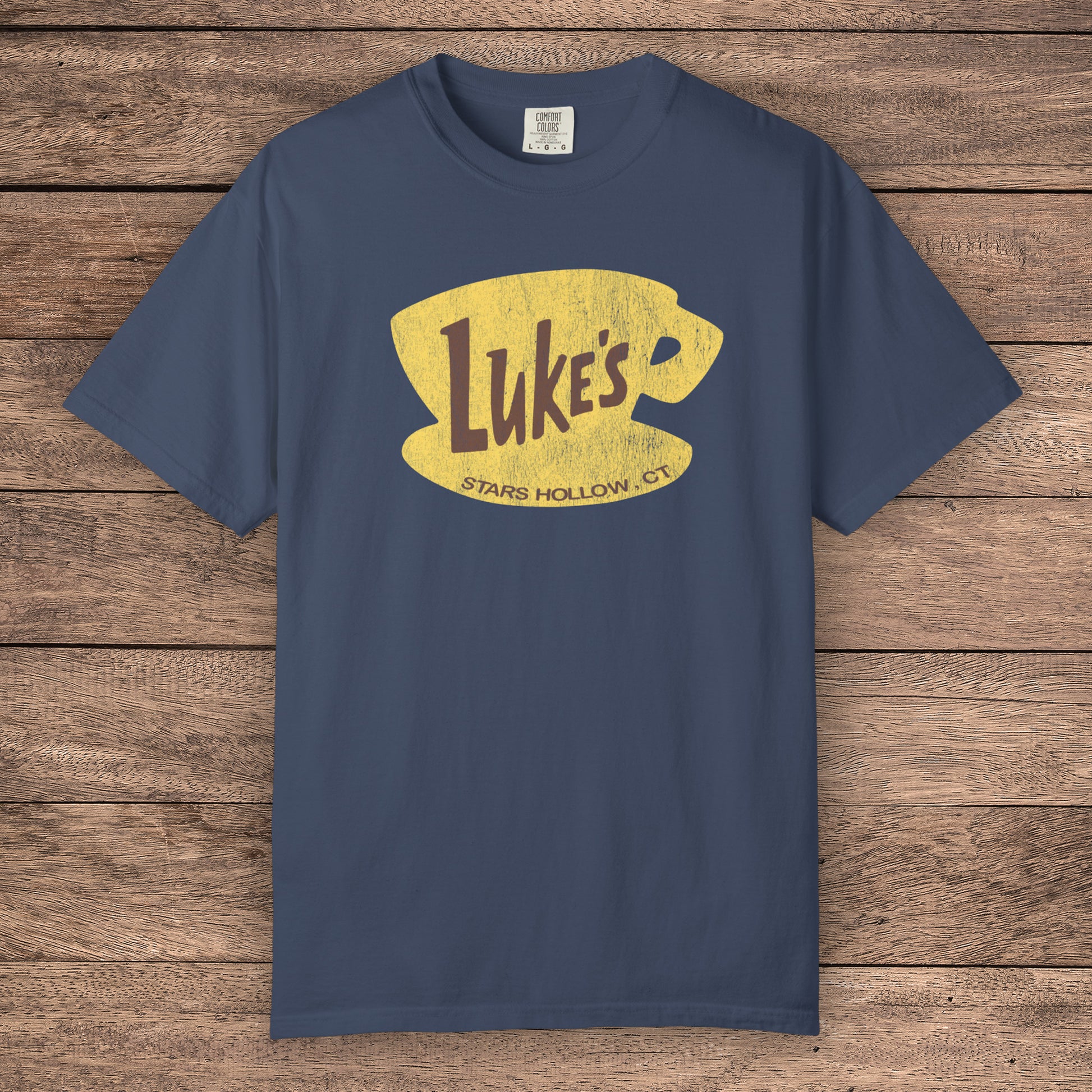 Midnight blue Comfort Colors t-shirt with vintage yellow Luke’s Diner logo from Gilmore Girls, laid flat on wood background.