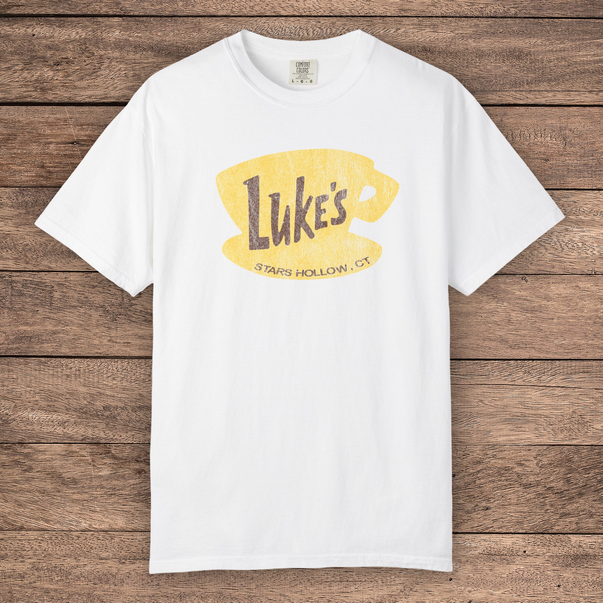 White Comfort Colors t-shirt with vintage yellow Luke’s Diner logo from Gilmore Girls, laid flat on wood background.