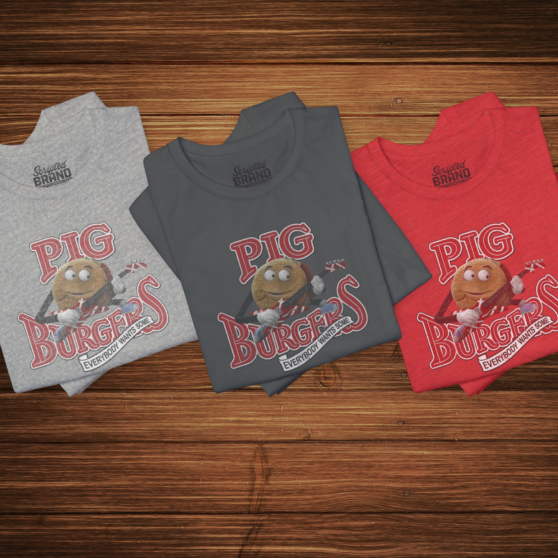Group of 3 folded soft Bella+Canvas 3001 short-sleeve t-shirts featuring a graphic of the fictional Pig Burgers logo from the movie Better Off Dead, along with the Van Halen singing hamburger playing guitar, with the small subhead phrase EVERYBODY WANTS SOME. The graphic is designed in a vintage distressed style, sold by ScriptedBrand.