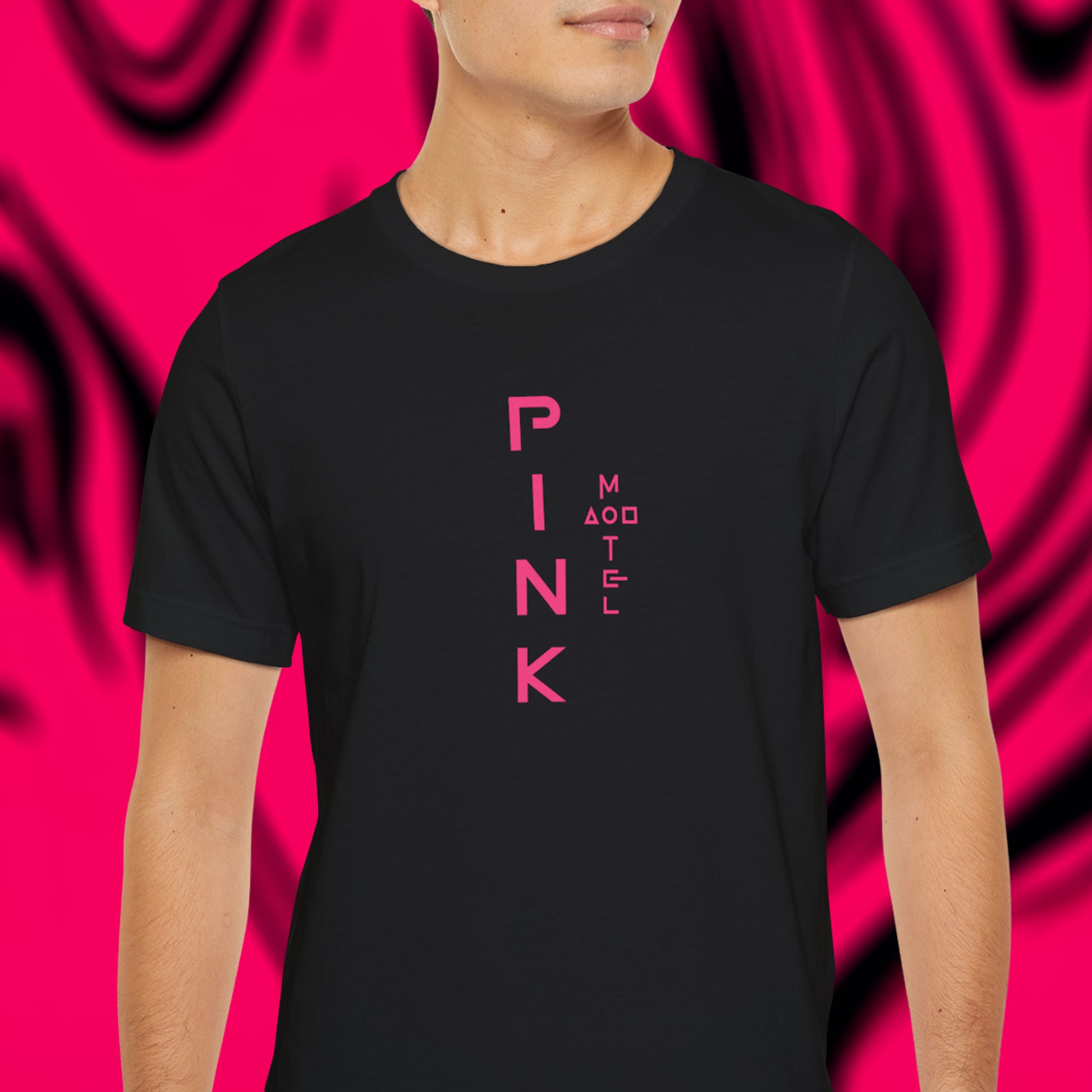 Male model wearing a black colored soft Bella+Canvas 3001 short-sleeve t-shirt featuring a pink logo graphic of the fictional Pink Motel inspired by the TV series Squid Game, in a vintage distressed style, sold by ScriptedBrand.