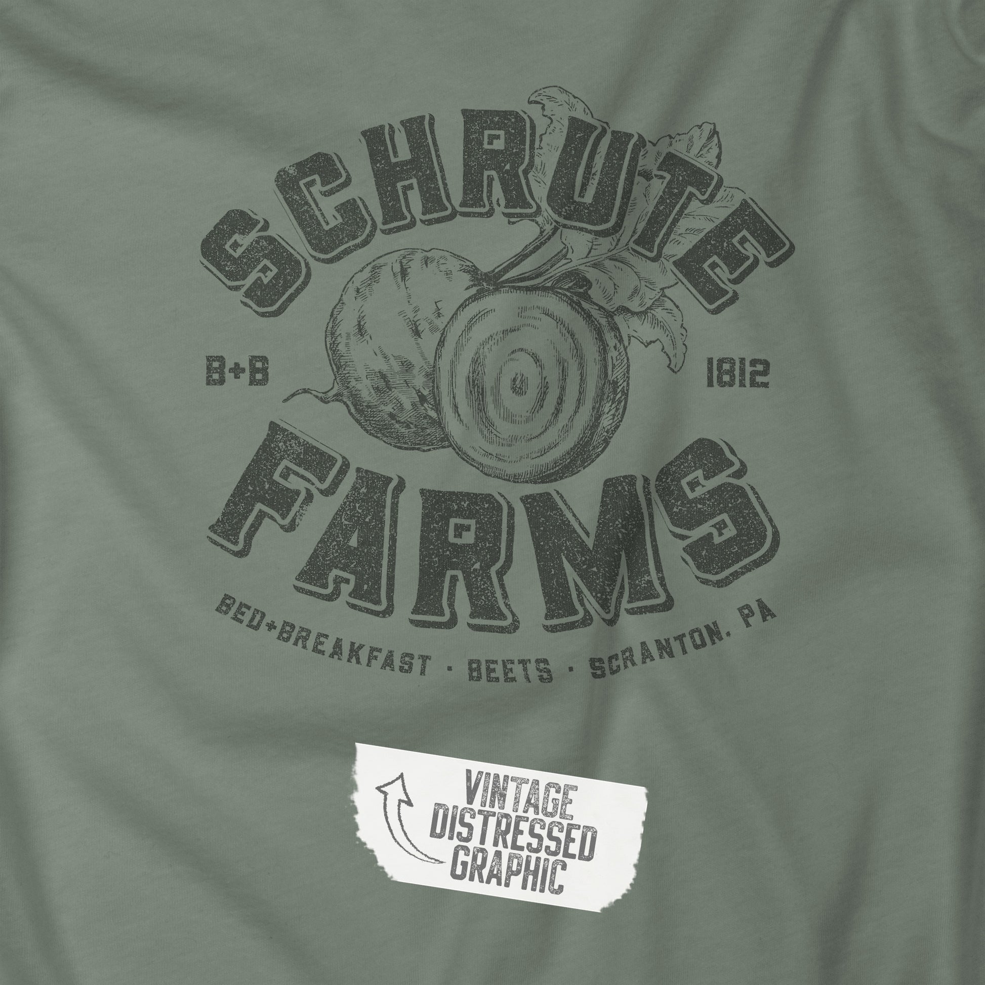 Closeup of Sage green t-shirt featuring a Schrute Farms logo from the TV show The Office designed by ScriptedBrand in a vintage distressed style.