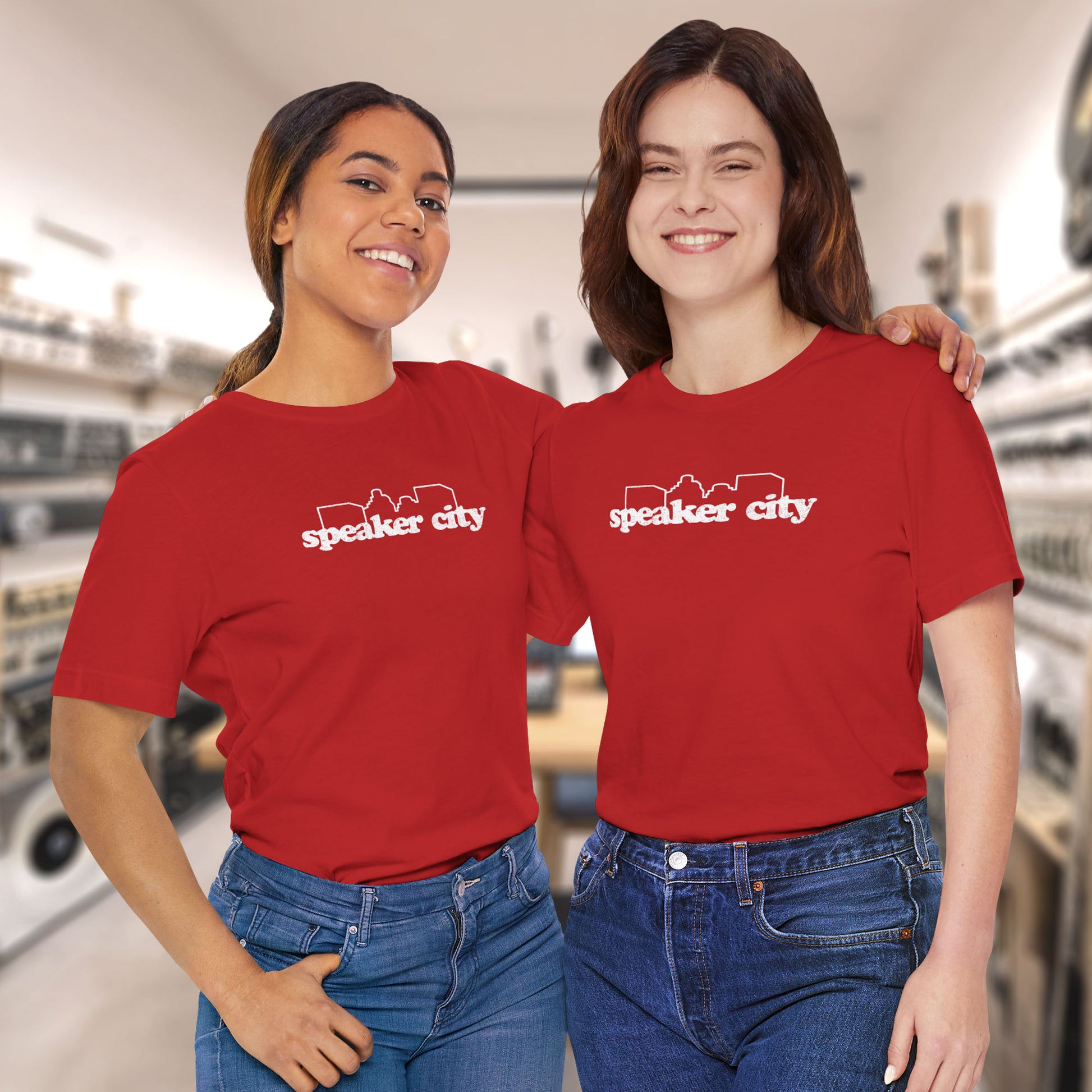 2 models wearing red t-shirts featuring the Speaker City logo from the movie Old School in a vintage distressed style with white print and skyline outline.