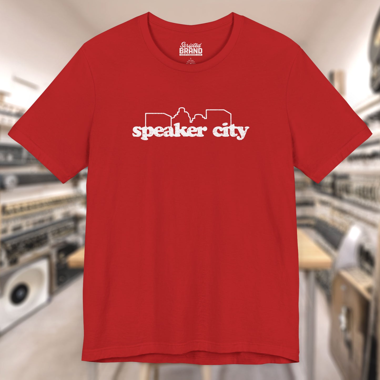 Front view of red t-shirt featuring the Speaker City logo from the movie Old School in a vintage distressed style with white print and skyline outline.