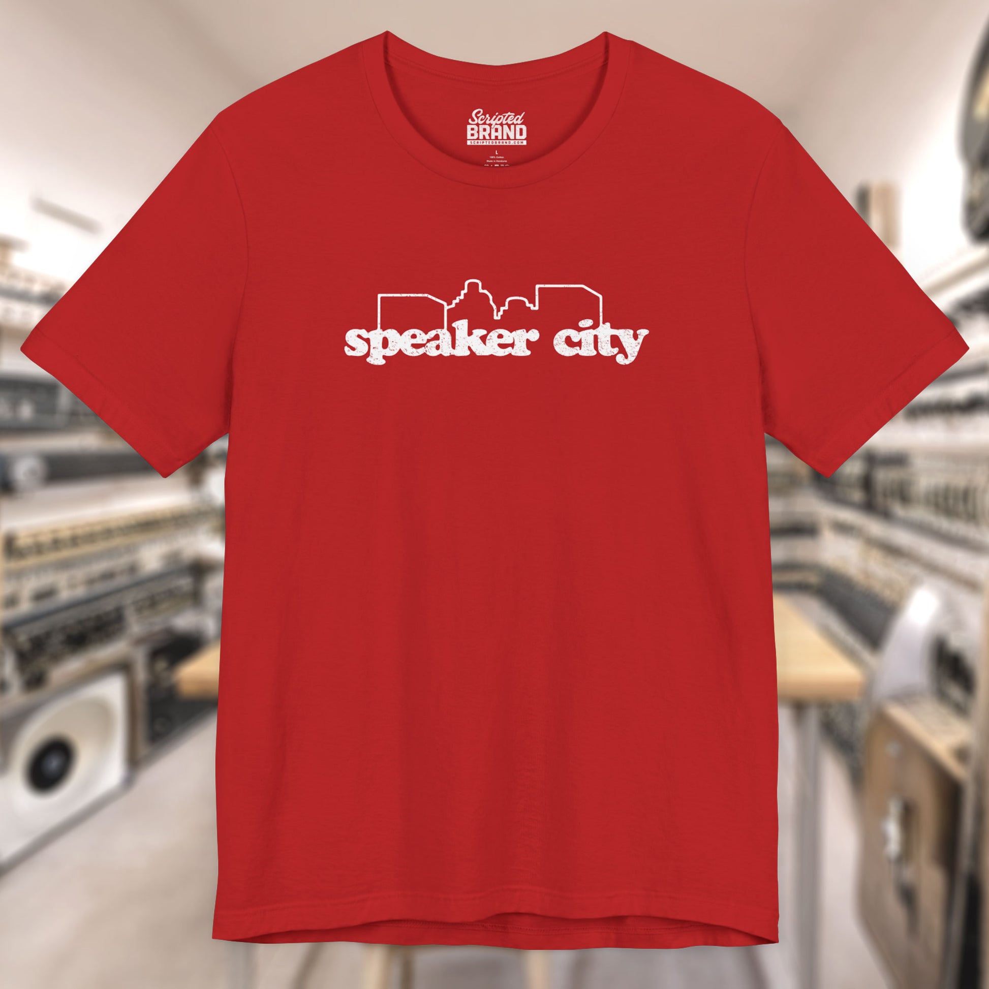 Front view of red t-shirt featuring the Speaker City logo from the movie Old School in a vintage distressed style with white print and skyline outline.