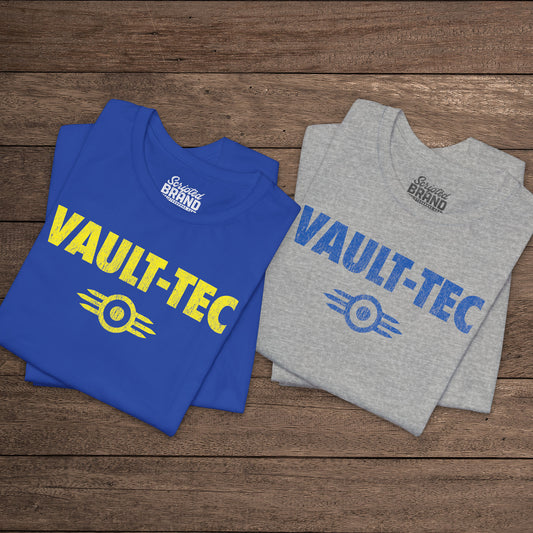 Two folded t-shirts featuring the Vault-Tec logo graphic from the video game Fallout in a vintage distressed style. 