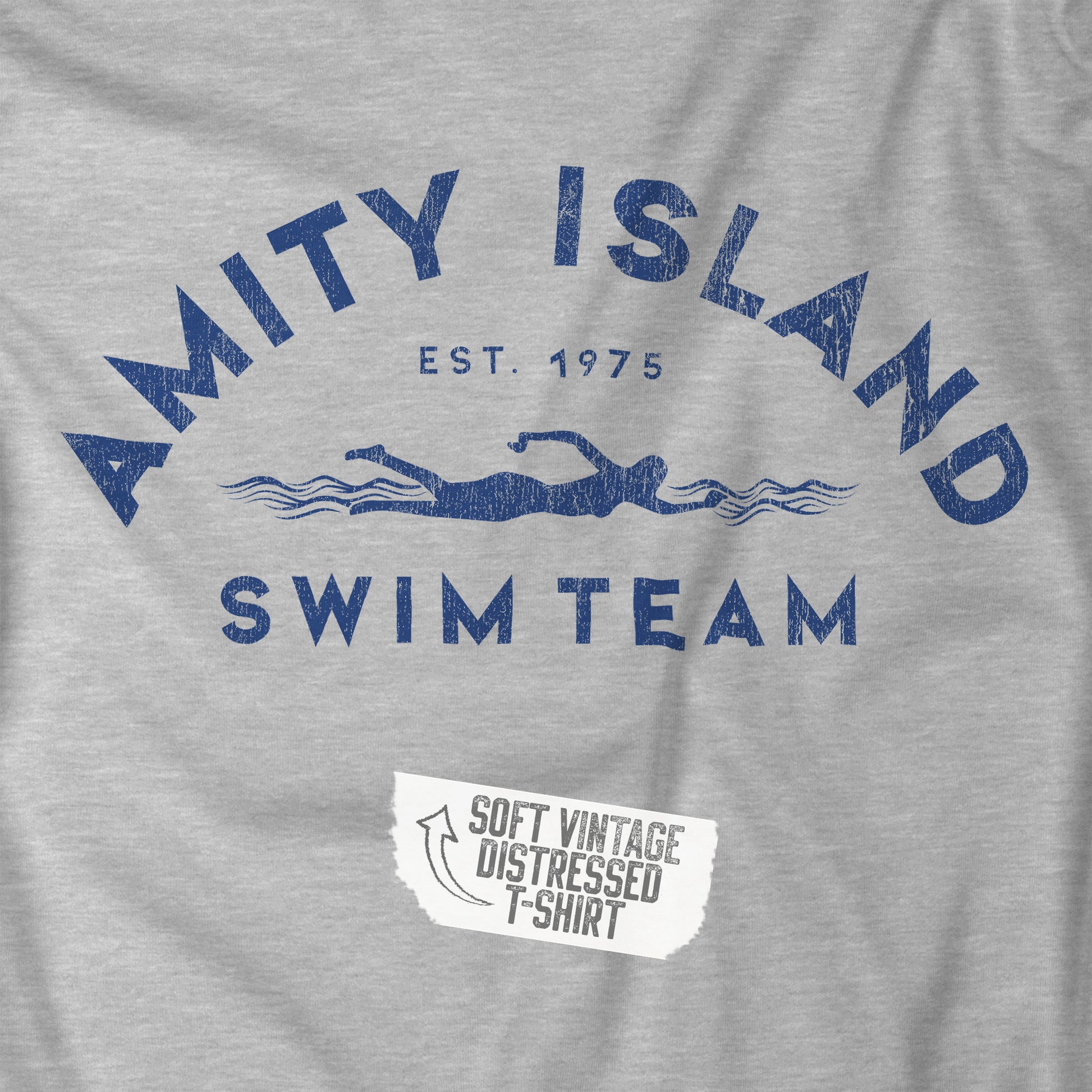 Closeup view of an athletic heather grey colored Soft unisex Youth Sizes Bella+Canvas 3001Y short-sleeve t-shirt featuring an Amity Island Swim Team logo graphic, designed by ScriptedBrand, and  inspired by the movie Jaws in a vintage distressed style.